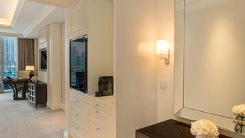 A hotel room with a large mirror, a dark wooden console table with a vase of flowers, a flat-screen TV, and a coffee machine.