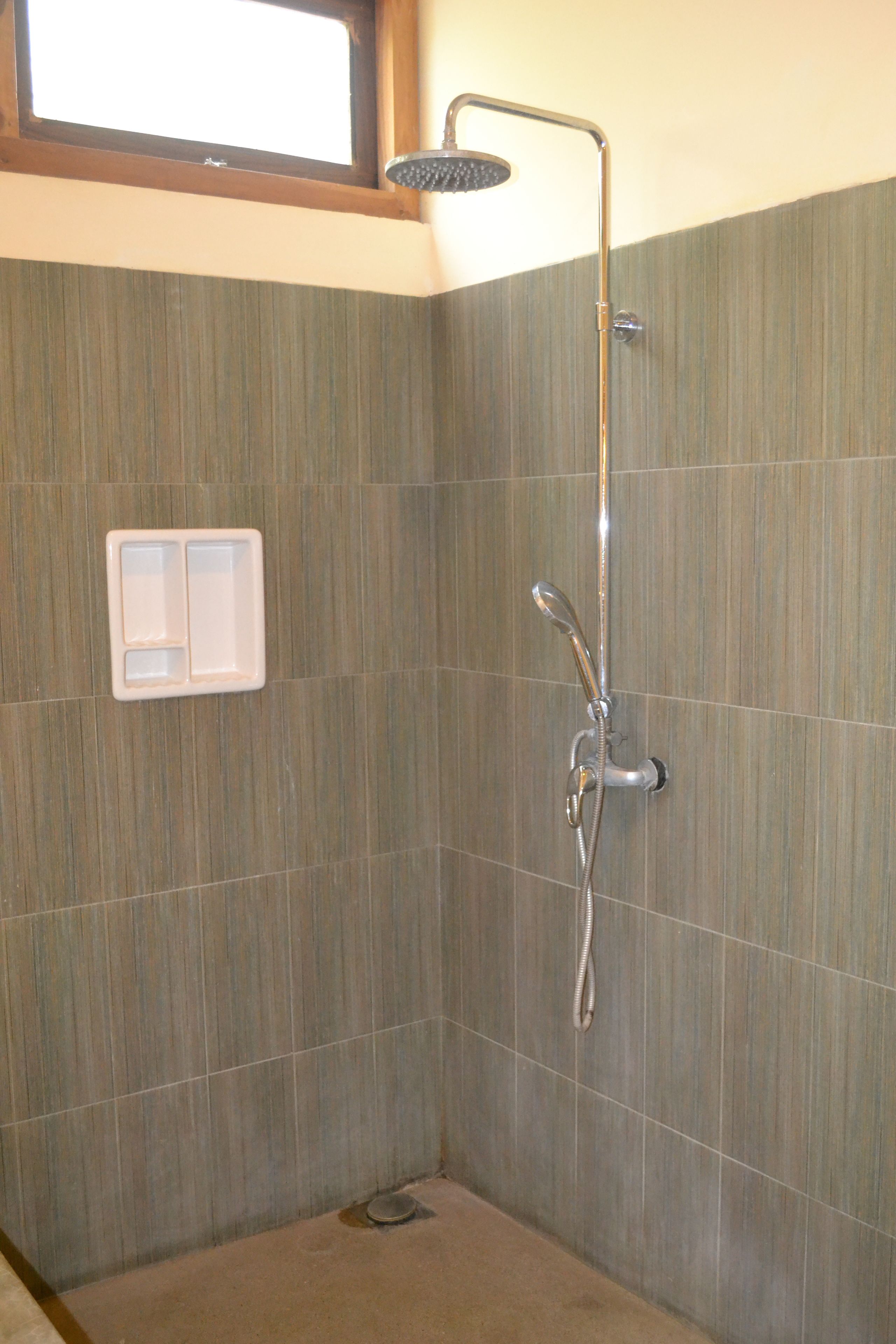 Un espacio de ducha con ducha de mano, panel de control en la pared y ventana superior.