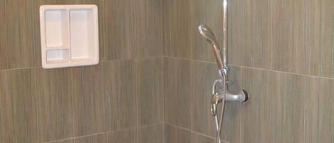Un espacio de ducha con ducha de mano, panel de control en la pared y ventana superior.