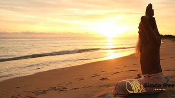 A person meditating on a yoga mat on a beach at sunset.
