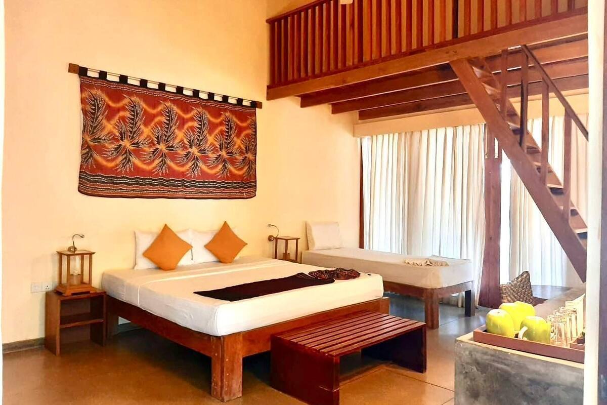 Ein Schlafzimmer mit einem großen Bett, einem Holz-Kopfteil, einer hölzernen Bank, einem Nachttisch, einer Wanddekoration und einer Treppe.