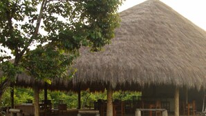A thatched-roof structure with outdoor seating and a grassy area in front.
