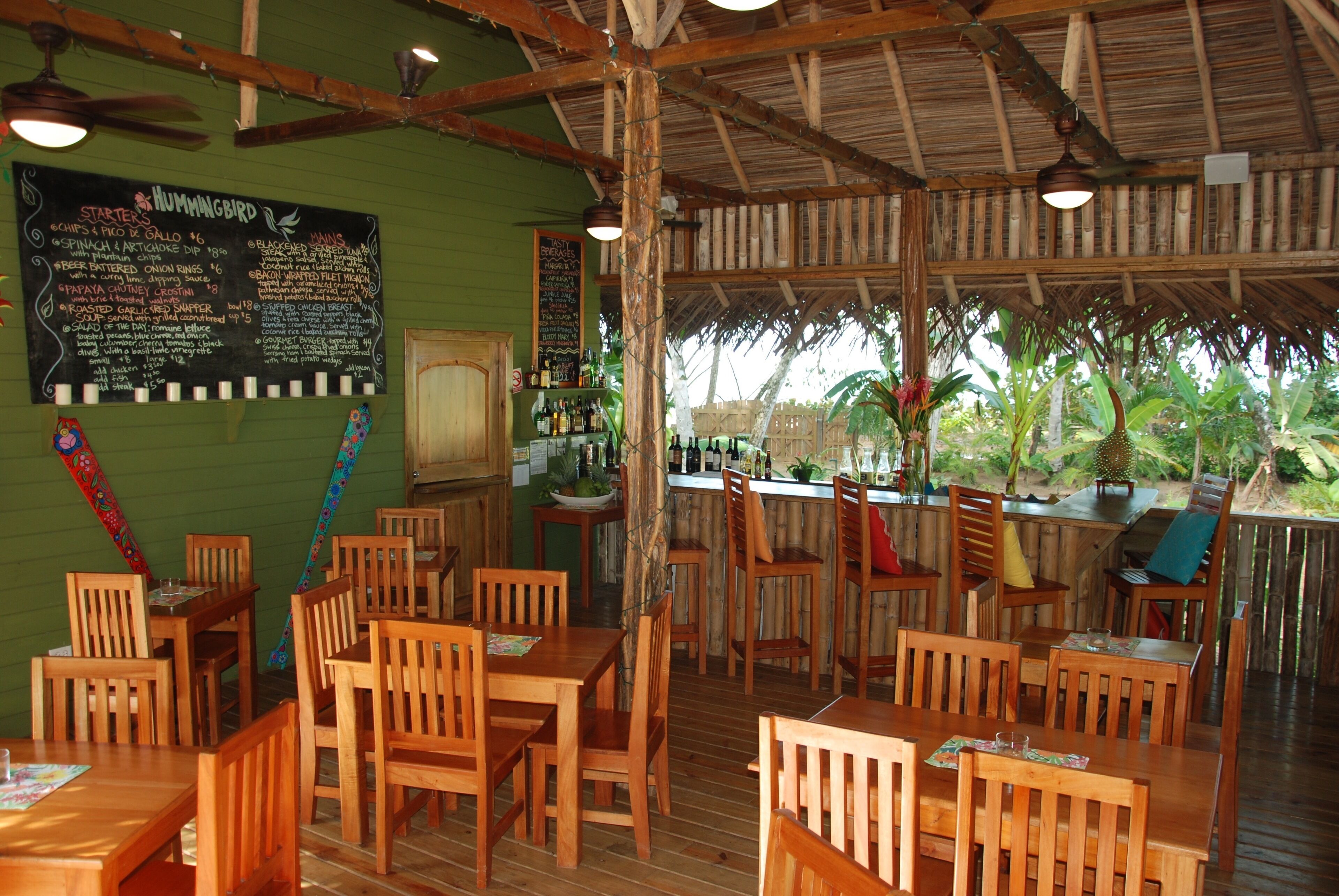 A restaurant with wooden tables and chairs, a chalkboard menu, and a bar area.