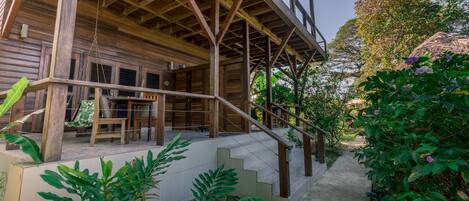 A wooden cabin with a covered porch, a staircase leading to a second level, and a garden area with plants and a pathway.