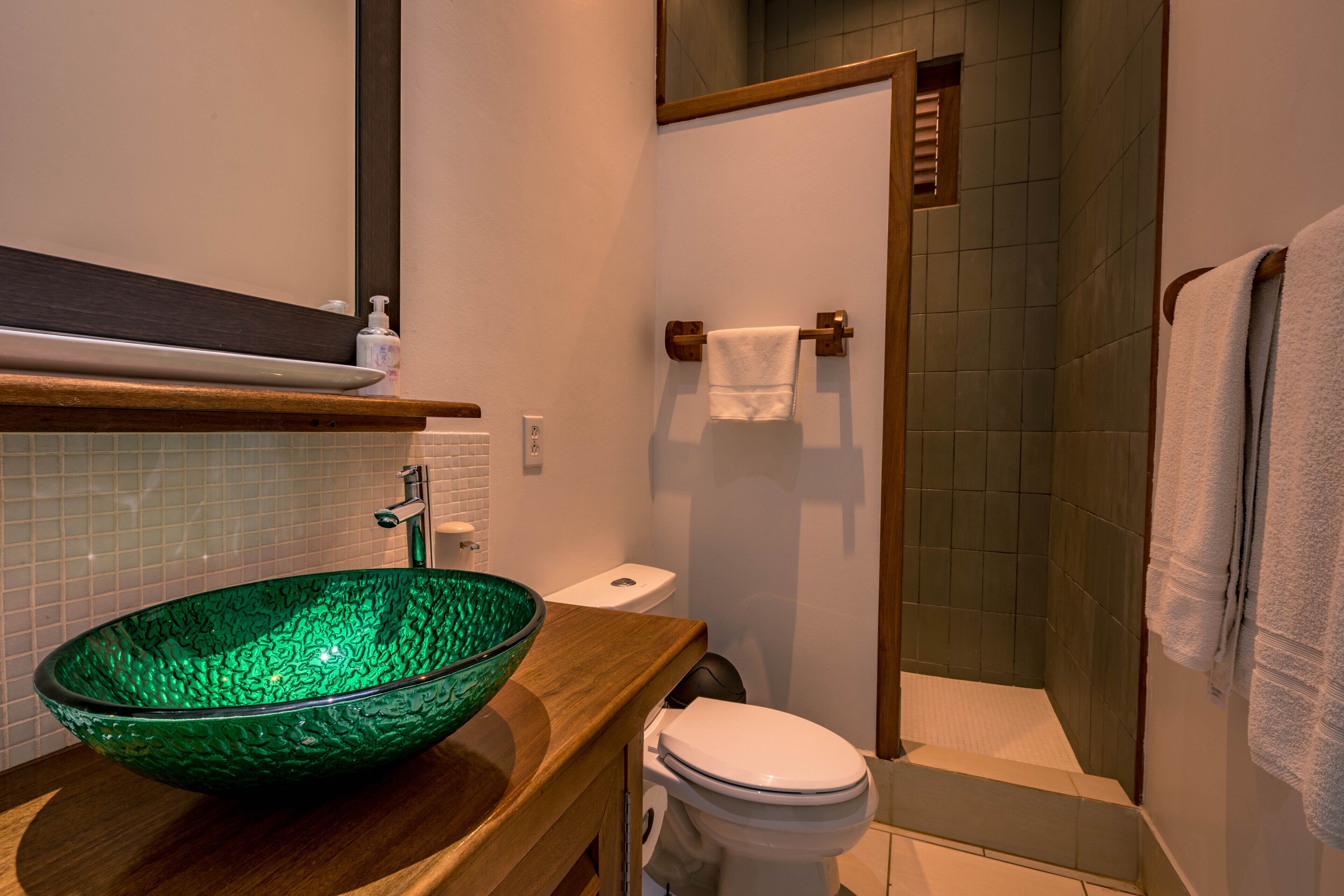 Ein Badezimmer mit einem grünen Waschbecken aus Glas, einer weißen Toilette und einer Duschkabine.