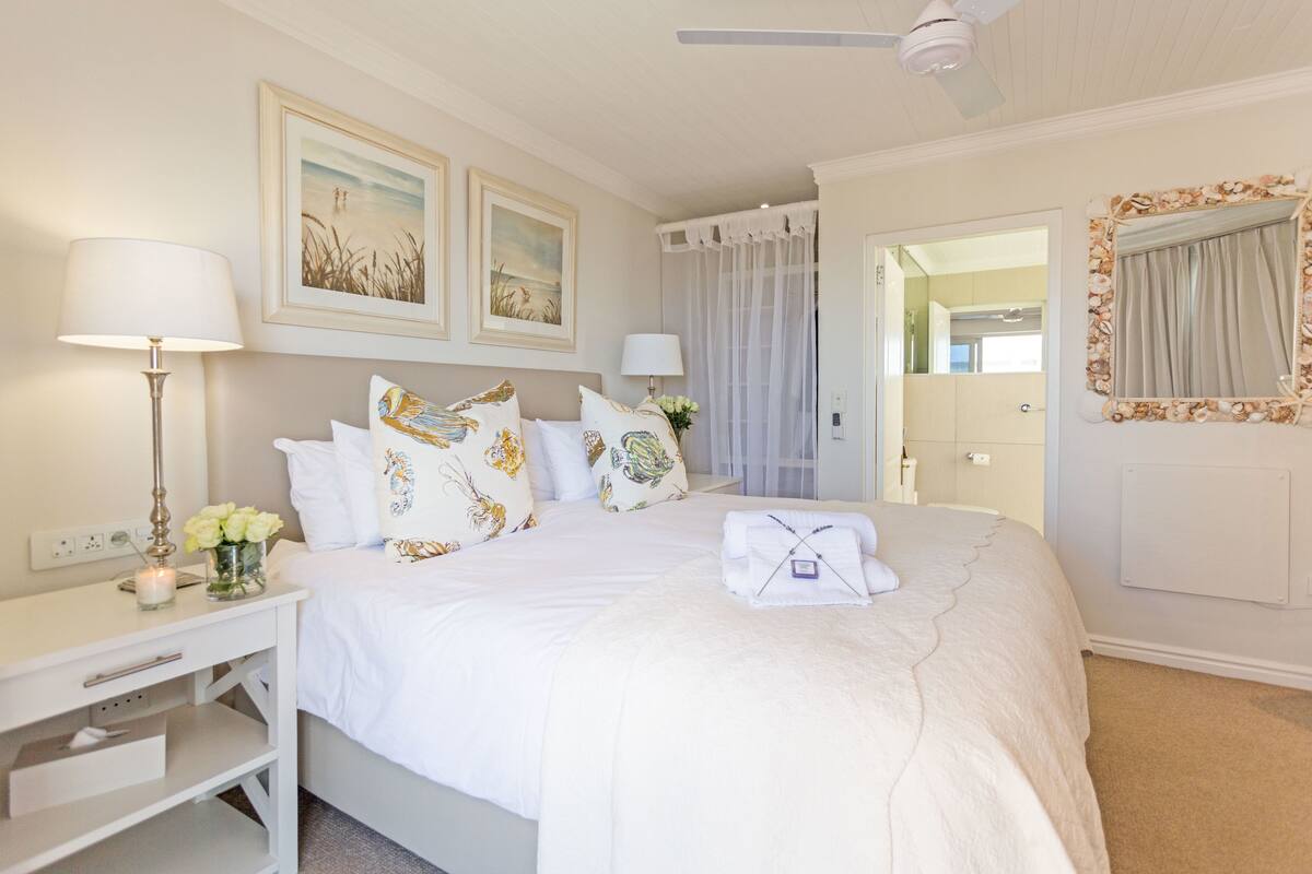 A neatly arranged bedroom with a bed, bedside table, lamp, and artwork on the wall.