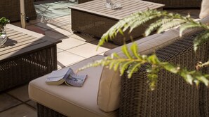 A wicker sofa with cushions, a wooden table, and a large umbrella in a patio area with a view of the ocean. - Ocean Watch Guest House (Plettenberg Bay)
