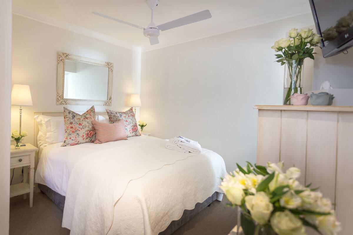A bedroom with a bed, a nightstand, a mirror, a ceiling fan, and a dresser.