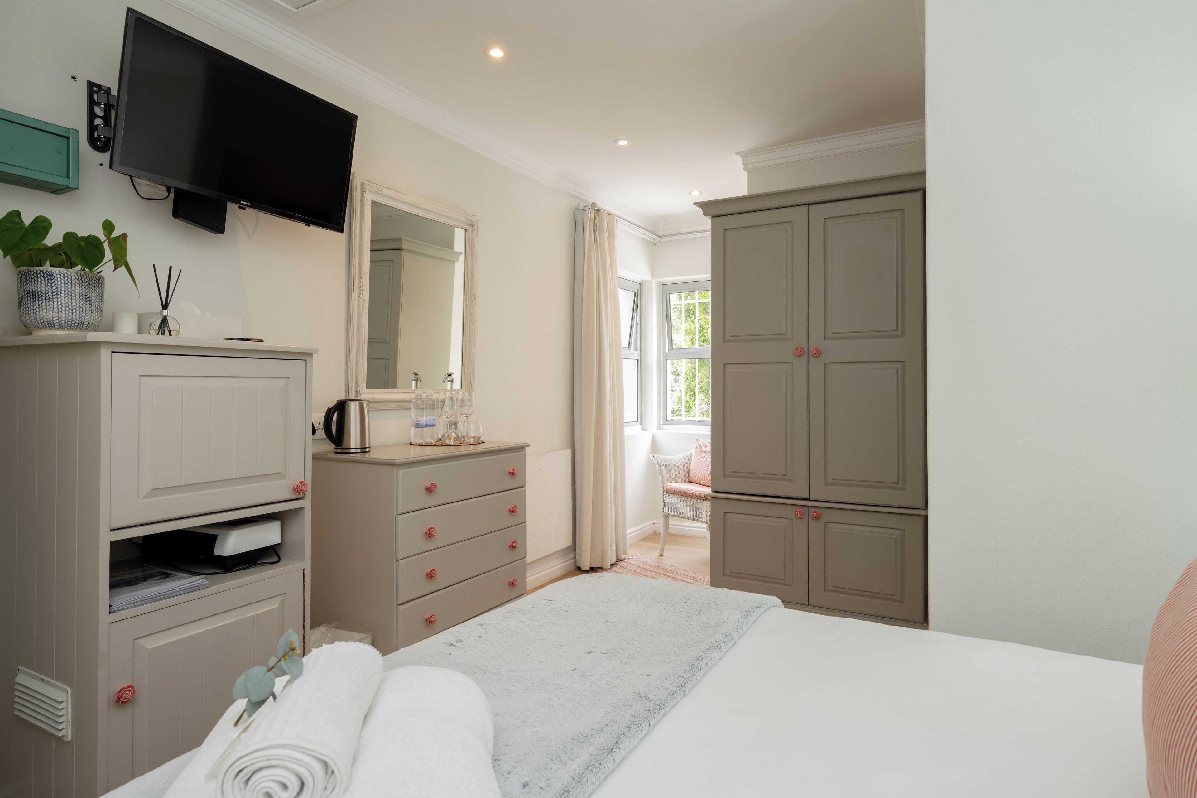 Un dormitorio con cama, cómoda, espejo y televisor montado en la pared.