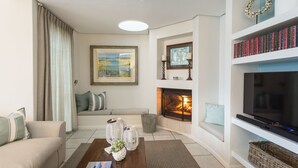 A living room with a sofa, a fireplace, a television, and a bookshelf. - Ocean Watch Guest House (Plettenberg Bay)