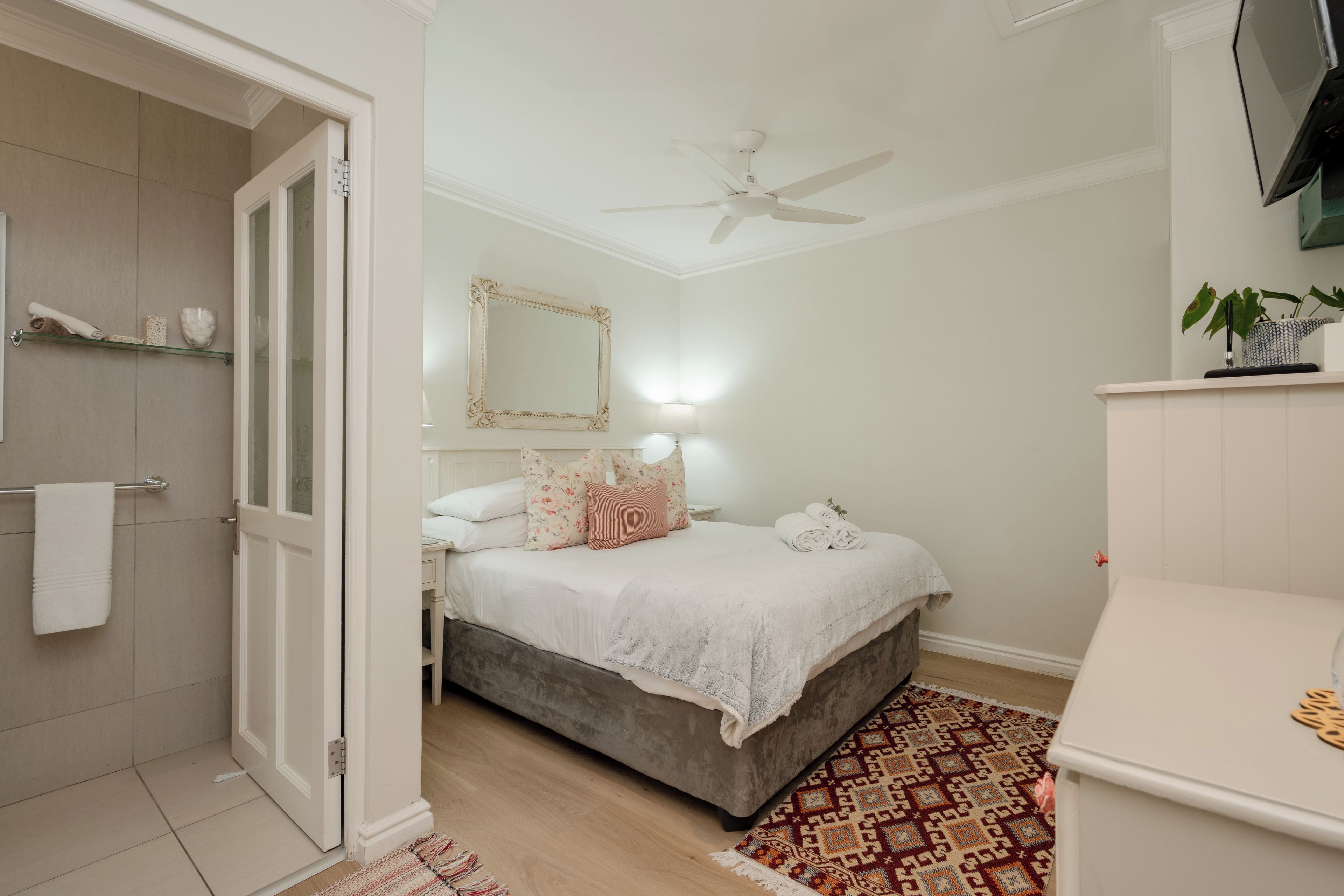 Ein Schlafzimmer mit Bett, Nachttisch, Spiegel, Deckenventilator und einem Badezimmer inklusive Handtuchhalter.
