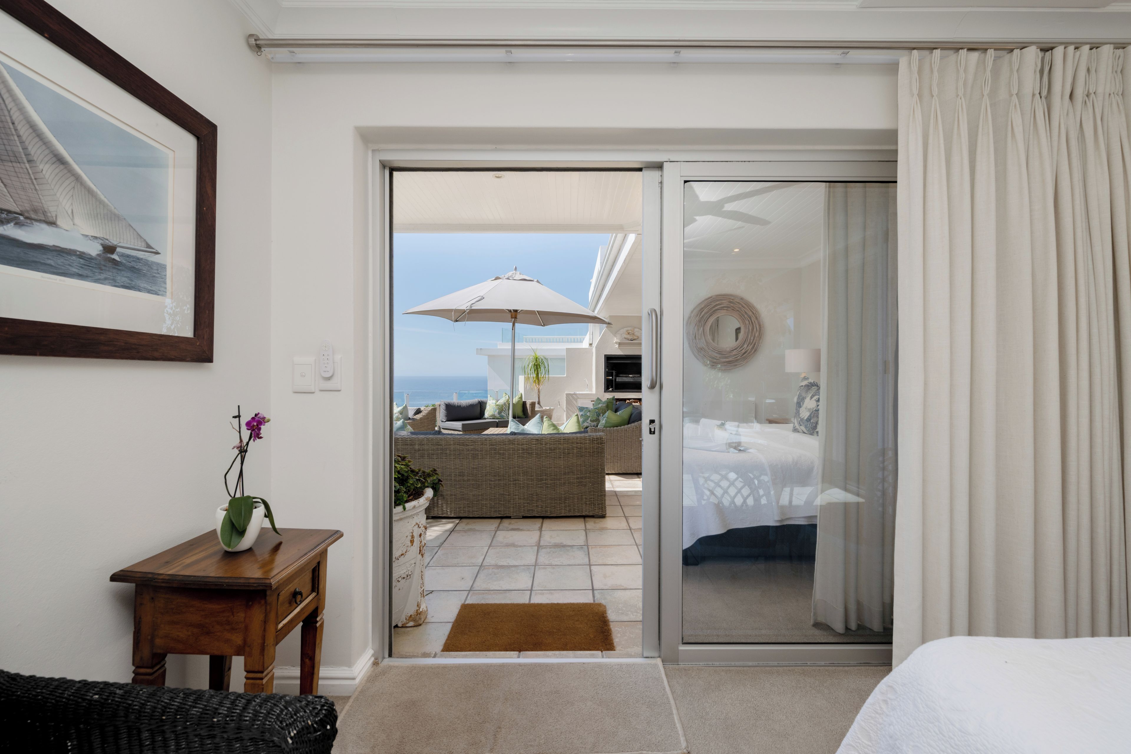 Une chambre d’hôtel dotée d’une porte-fenêtre coulissante donnant sur un espace extérieur aménagé avec une table, des chaises et un parasol.
