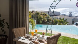 Una mesa de comedor con alimentos para el desayuno y vistas a una piscina y al océano.