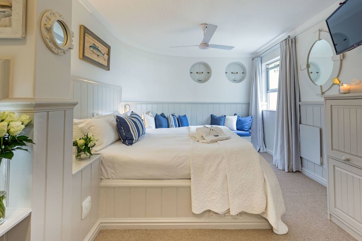 A bedroom with a bed, a ceiling fan, a TV, and a window with curtains.