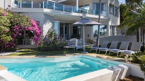 A swimming pool with lounge chairs, a covered seating area, and a balcony overlooking the pool. - Ocean Watch Guest House (Plettenberg Bay)