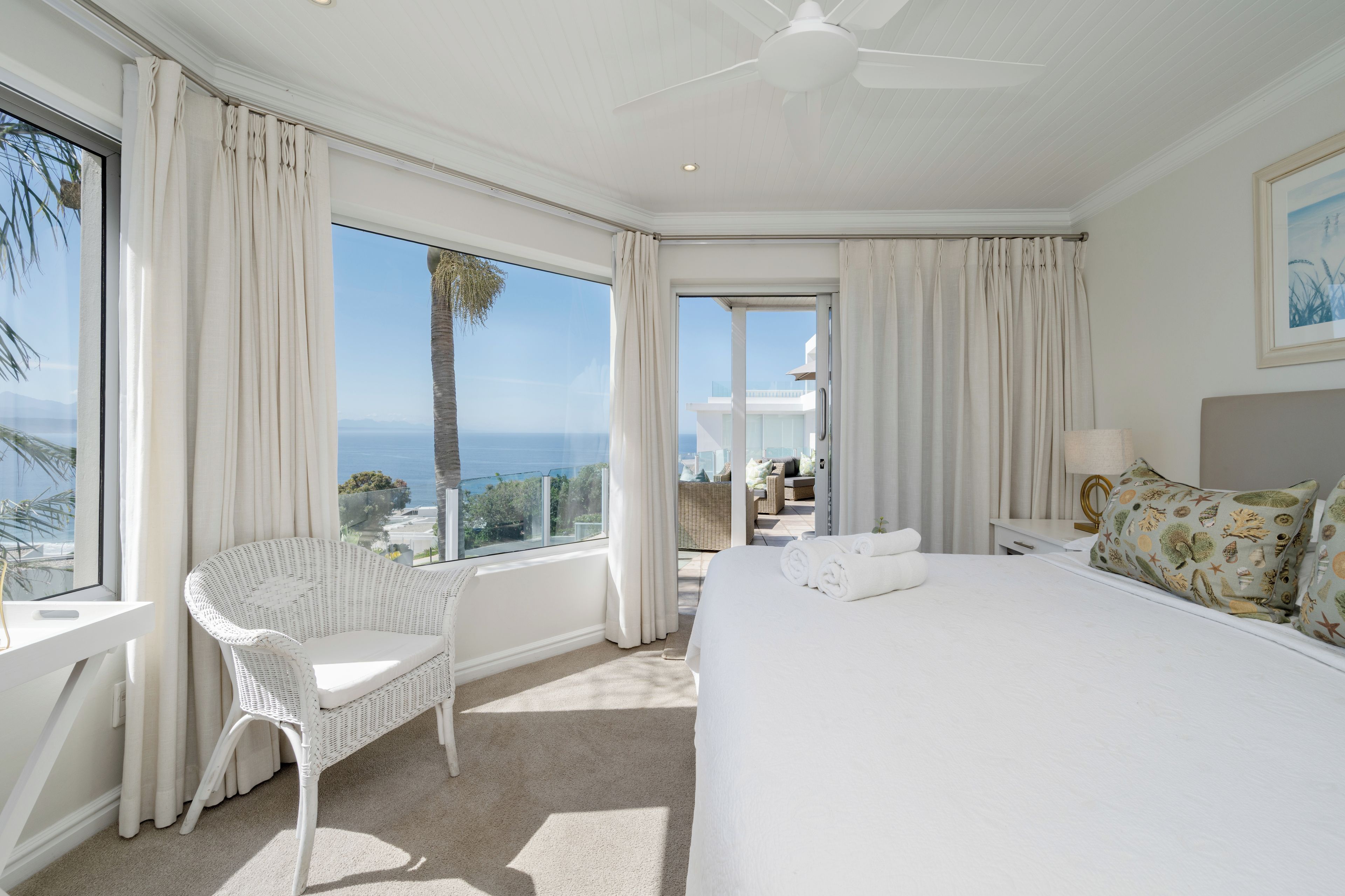 Habitación de hotel con una cama grande, una silla, un balcón con vista al mar y un ventilador de techo.
