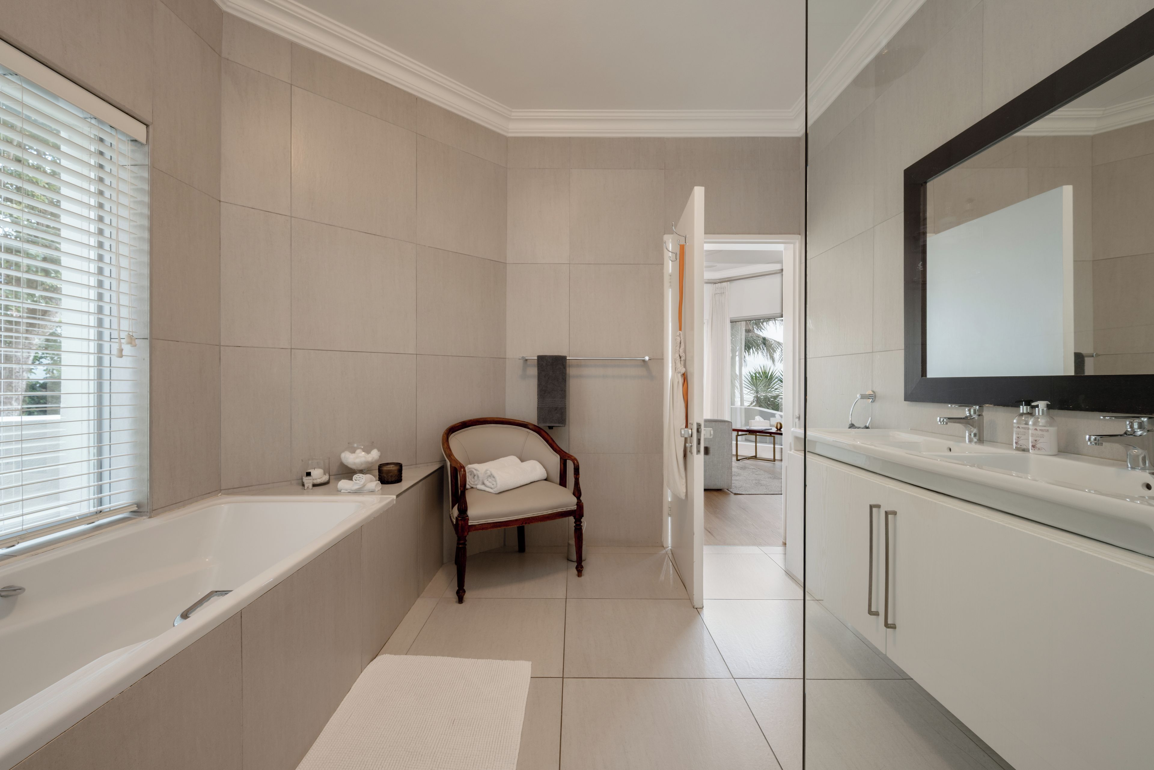 A modern bathroom with a bathtub, a wooden chair, and a large mirror.