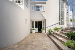 A narrow courtyard with a staircase leading to a door, surrounded by white walls and potted plants. - Ocean Watch Guest House (Plettenberg Bay)