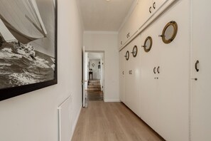 Um corredor com um grande quadro de temática náutica, piso de madeira e um conjunto de armários brancos com puxadores circulares.