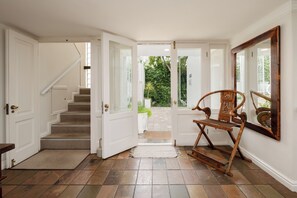 A staircase leading to a door with a view of a garden. A wooden chair and a mirror are visible. - Ocean Watch Guest House (Plettenberg Bay)
