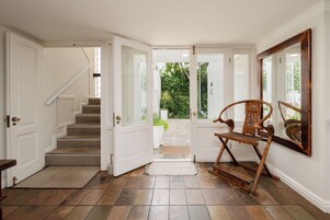 Una escalera conduce a una puerta con vista a un jardín. Se ve una silla de madera y un espejo.
