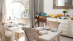 Un comedor con sillas de mimbre, una mesa blanca con platos, fuentes y un florero con flores.