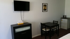 Une chambre d’hôtel comprenant un lit, un bureau avec une chaise, un téléviseur fixé au mur, un petit réfrigérateur et un tableau encadré au mur.