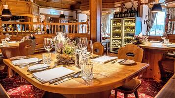 A restaurant with wooden interiors, a central dining table set with plates, cutlery, and glasses, surrounded by chairs.