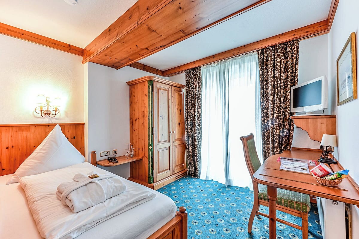 Een hotelkamer met een bed, een bureau met televisie, een kledingkast en een raam met gordijnen.