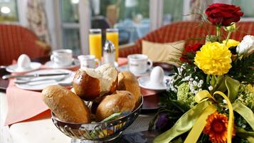Impostazione colazione con pane, succo e fiori su un tavolo.