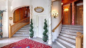 A grand staircase with a wooden handrail, a red patterned carpet, and a sign above the door. - Schloss Hotel Holzrichter (Nachrodt-Wiblingwerde)