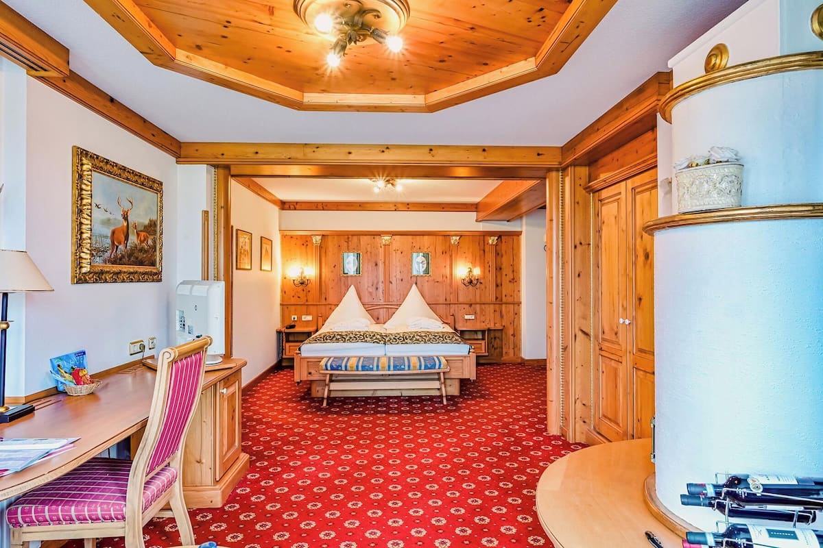 Een hotelkamer met een houten plafond, een rood karpet met een patroon, een bed met een gestreept dekbed en een groot cilindrisch object aan de rechterkant.