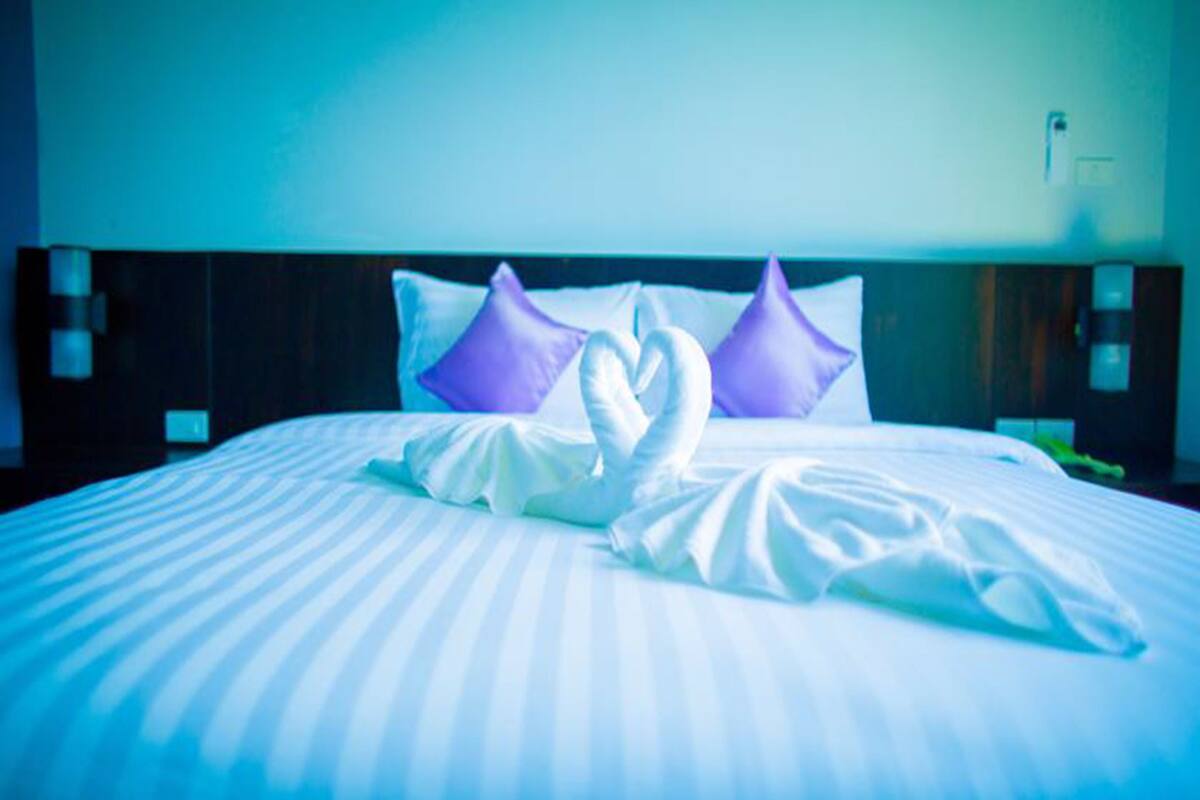 A hotel room with a neatly made bed, two purple pillows, and a heart-shaped towel arrangement.
