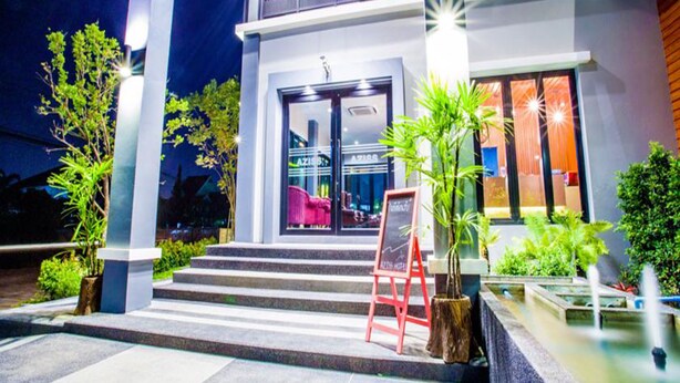 Una entrada de hotel moderna con puerta de vidrio, asientos exteriores y una pequeña fuente de agua.