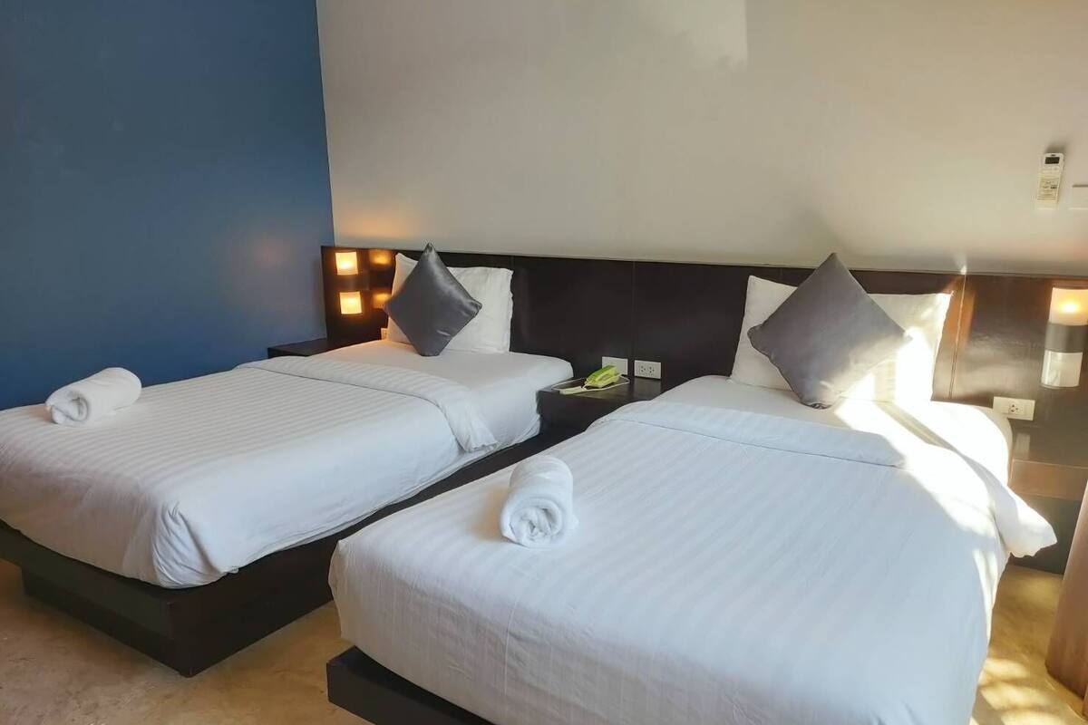A hotel room with two single beds, each with a pillow and a rolled towel.