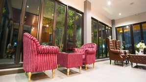 Un hall amplio con grandes puertas de vidrio, sillones tapizados en rojo y un sillón de cuero marrón.
