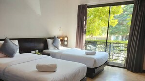 Habitación de hotel con dos camas, un ventanal con vistas a la vegetación y un balcón.