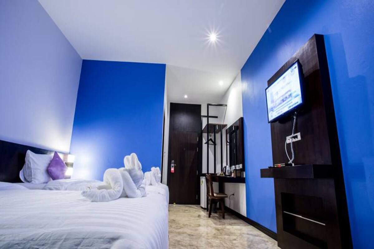 A hotel room with a large bed, a flat-screen TV mounted on the wall, a desk with a chair, and a mirror.