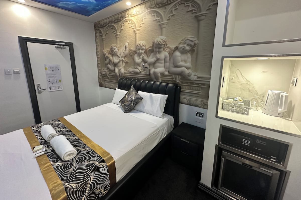 Une chambre d’hôtel comprenant un lit, une fresque au plafond, un mur orné de sculptures, un minibar et un four encastré.