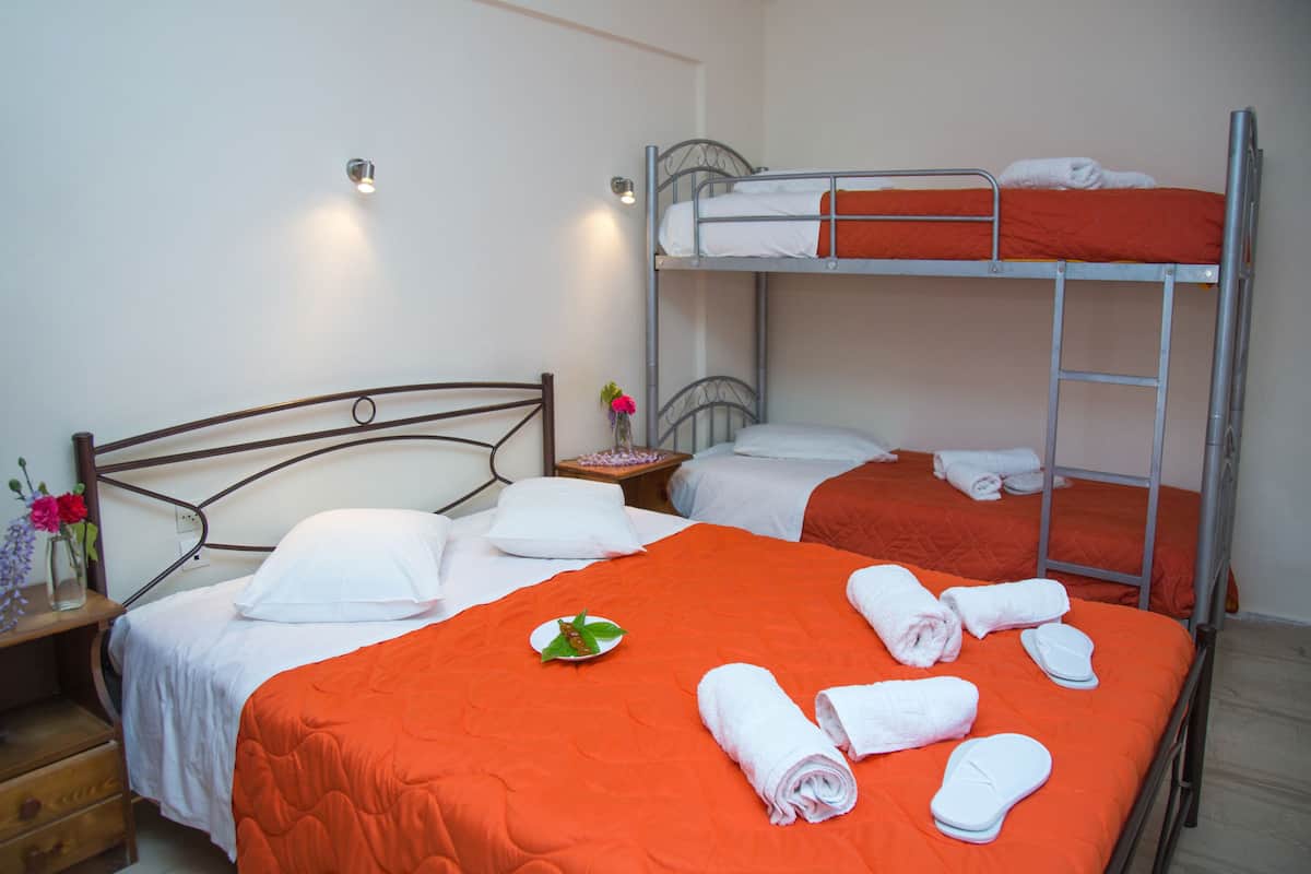 A hotel room with two beds, one with a wooden headboard and one with a metal bunk bed. There are towels and a plate with a leaf on the beds.