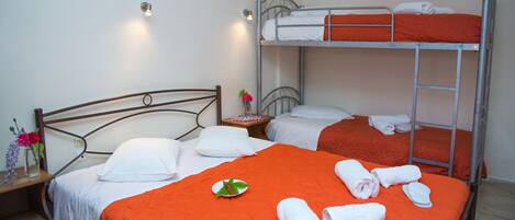 A hotel room with two beds, one with a wooden headboard and one with a metal bunk bed. There are towels and a plate with a leaf on the beds.