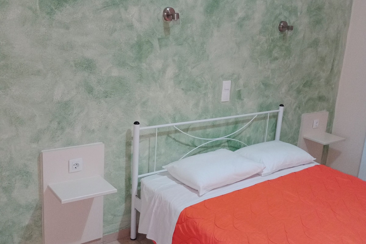 A single-bed room with a green textured wall, white bedside tables, and a red bedspread.