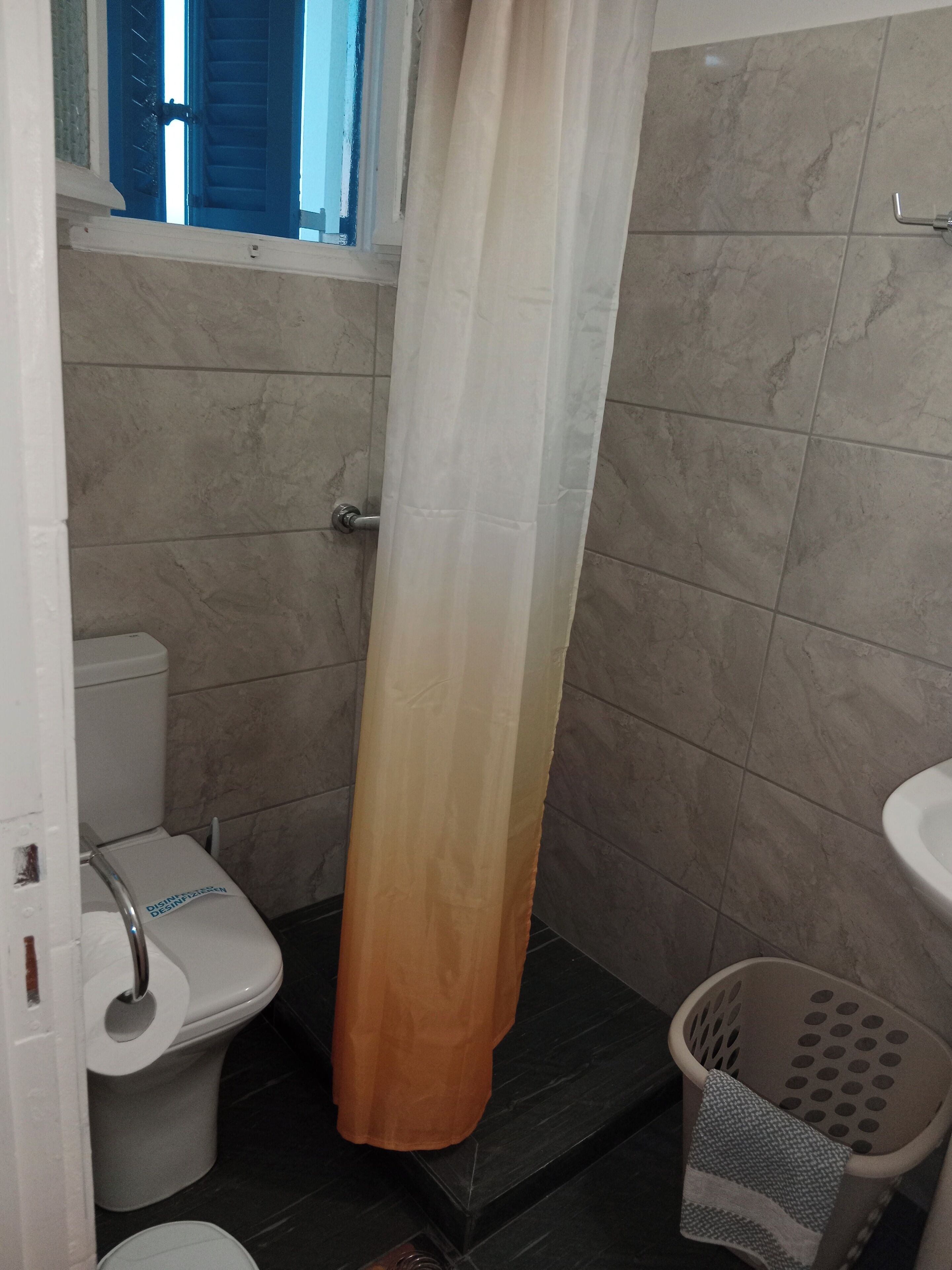 Une salle de bain équipée de toilettes, d’un rideau de douche, d’un lavabo et d’un panier à linge.