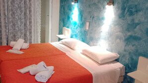 A hotel room with a large bed, two bedside tables, a nightstand, a window with curtains, and a blue textured wall. - Aristides Studios (Corfu)