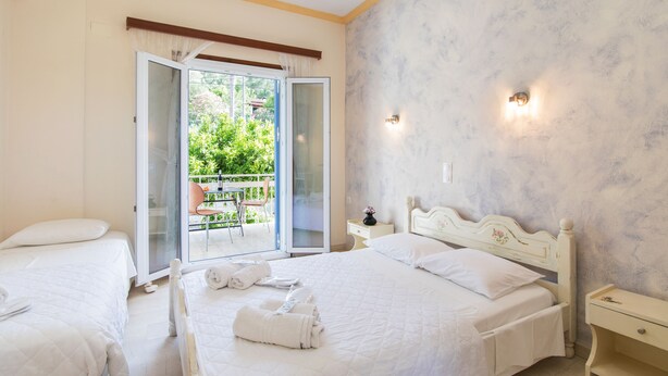 A bedroom with two beds, a balcony, and a view of greenery. - Aristides Studios (Corfu)