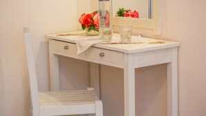 A bathroom vanity with a mirror, a vase of flowers, and a bottle of lotion. - Aristides Studios (Corfu)