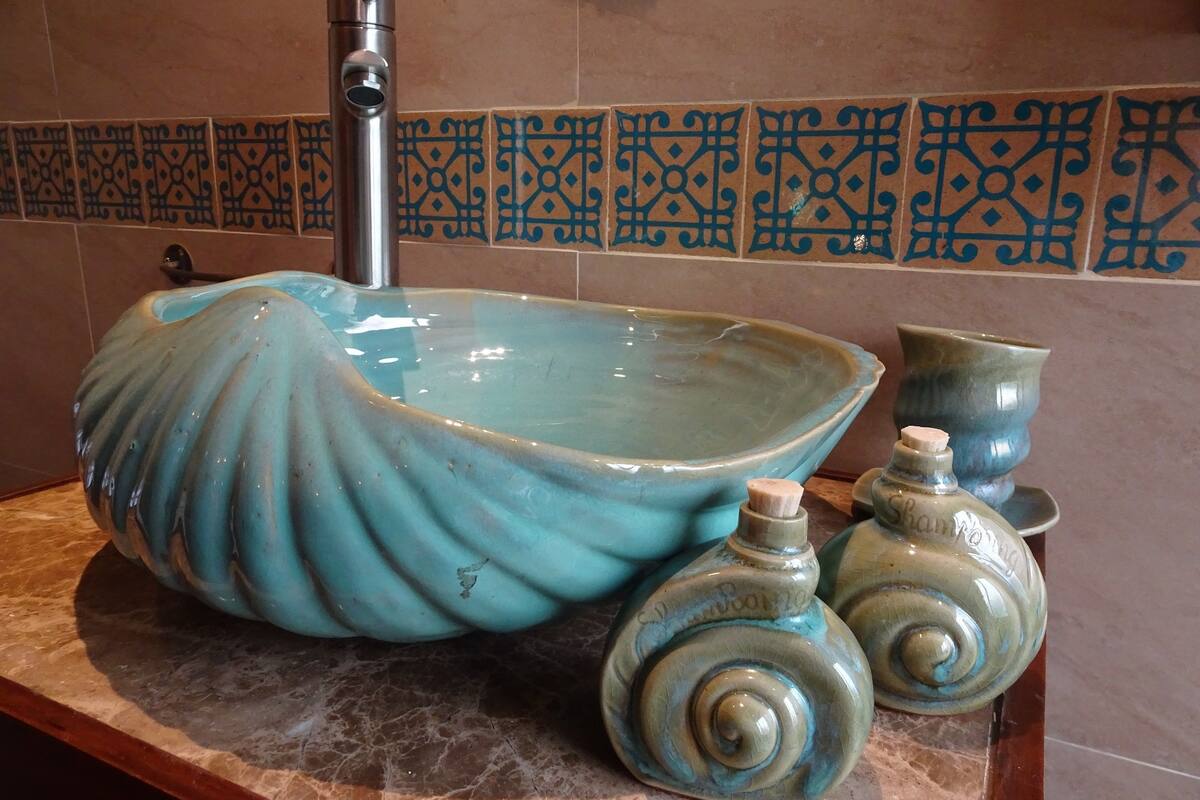 Un lavabo de salle de bain doté d’un grand bac de forme arrondie, de couleur bleue, et d’un robinet. On trouve deux vases en céramique assortis sur le comptoir.