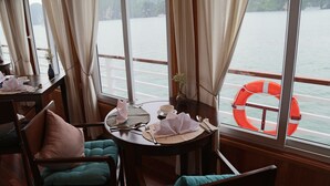 Un coin repas avec une table dressée pour deux personnes, un gilet de sauvetage posé sur le rebord de la fenêtre et une vue sur une étendue d’eau calme.