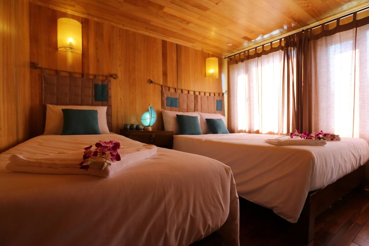 Une chambre d’hôtel avec deux lits, des boiseries et une table de chevet avec une lampe.