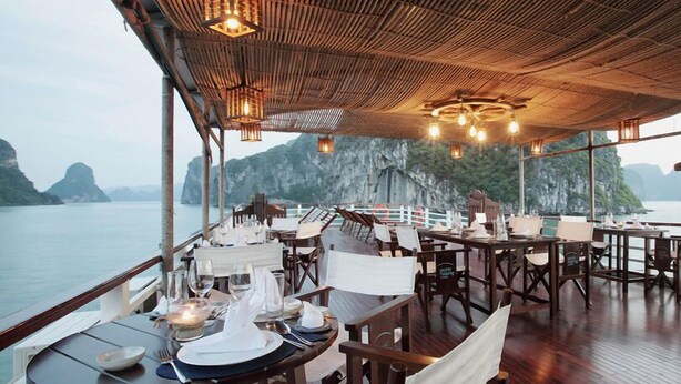 Un restaurant dont les tables sont dressées pour le service, offrant une vue sur un plan d’eau et des falaises.